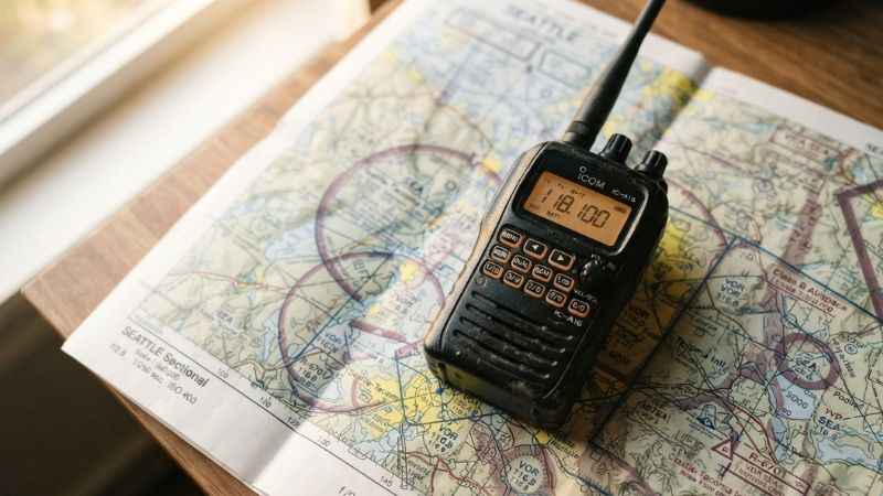 A handheld airband radio sitting on an aviation map displaying a voice communication frequency
