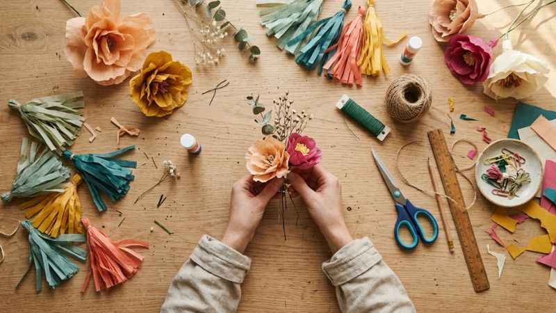 Hands crafting handmade paper party decorations and centerpieces on a clean rustic wooden table