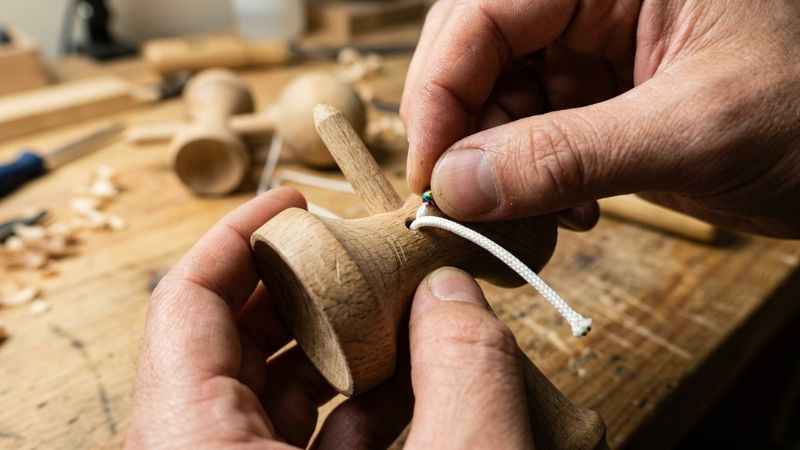 Hands threading a replacement string through the crosspiece of a wooden kendama.